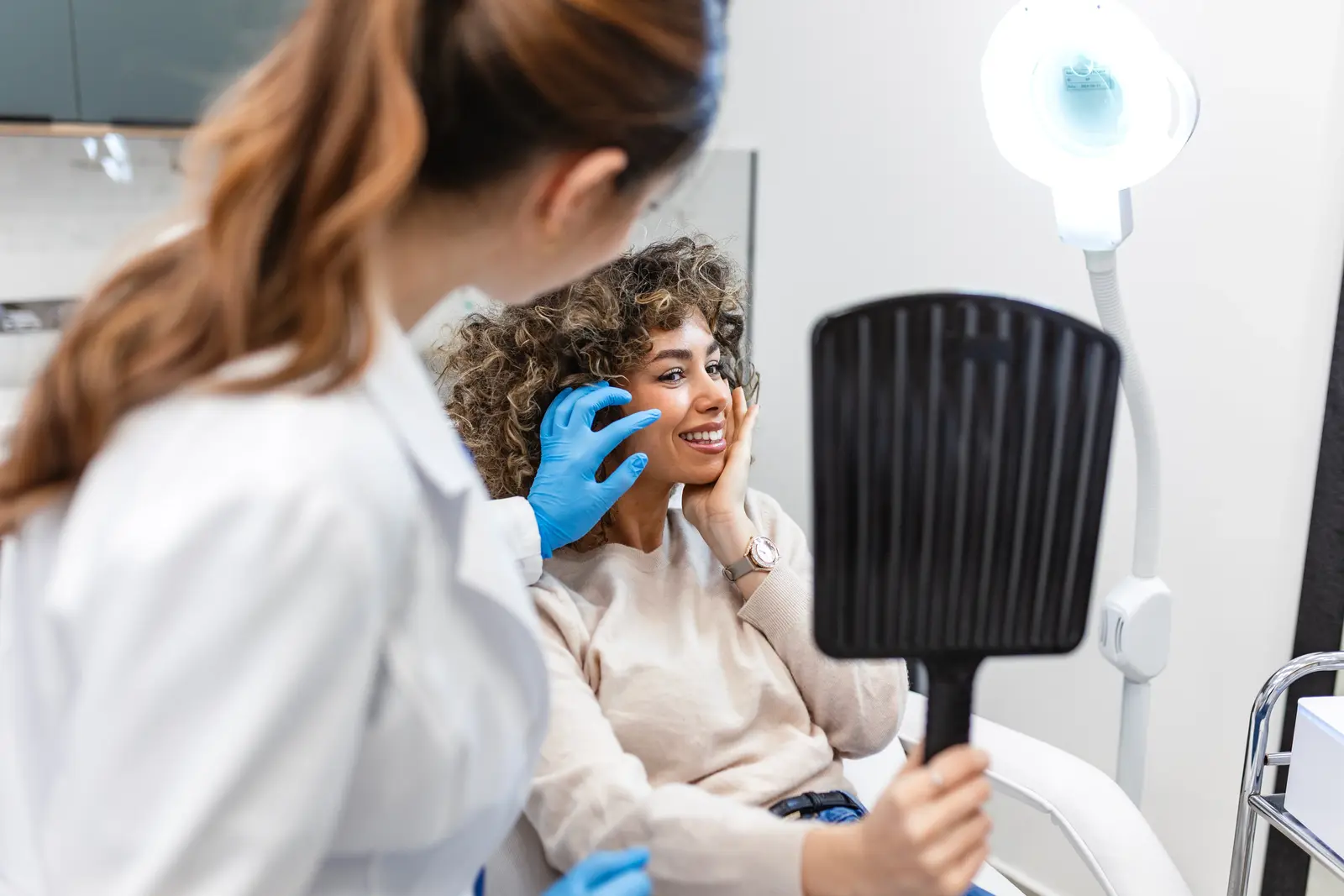 Patient checking facial treatment results in hand mirror during consultation.